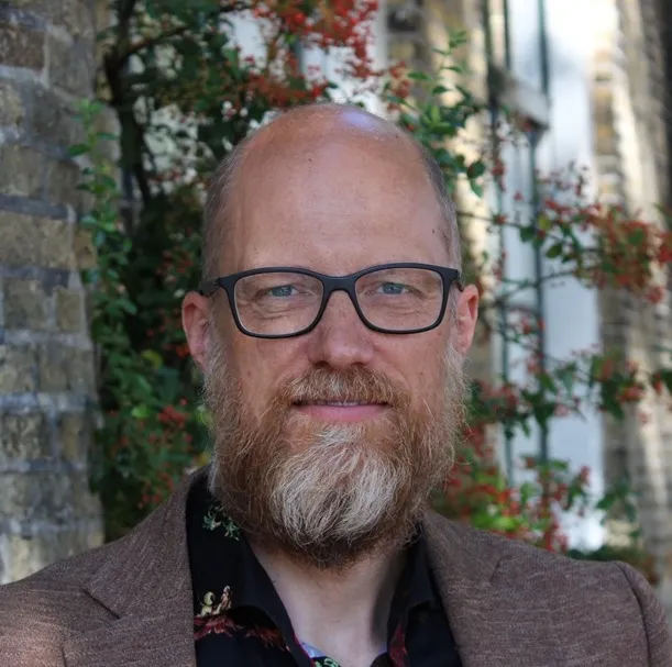 Christiaan kijkt naar links, staand voor een monumentaal gebouw in zwart-wit